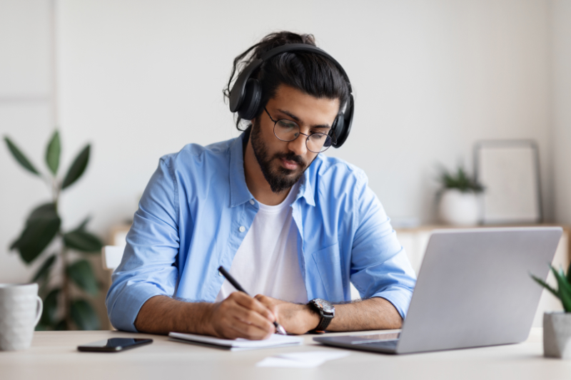 Man in Lafayette engrossed in work at his home office desk, wearing headphones, with vibrant plants in the background.