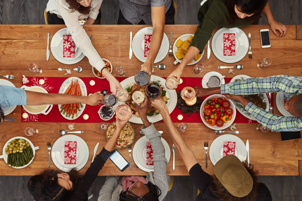 A diverse group of people seated around a kitchen table, enjoying a festive holiday meal together, showcasing the warmth and joy of gatherings in a beautifully designed kitchen space.